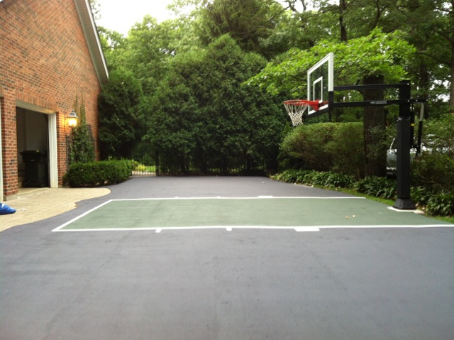 This half court playing area is on an asphalt concrete blacktop driveway in front of a 3 car garage.