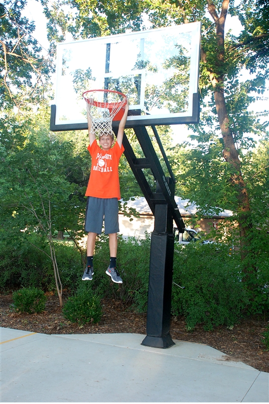 A young boy hangs on his Pro Dunk Diamond basketball hoop smiling. 