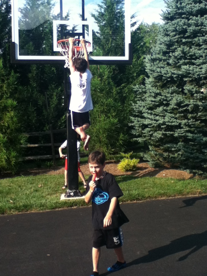 There is children on the asphalt concrete blacktop driveway, having fun with a Pro Dunk Platinum Basketball.
