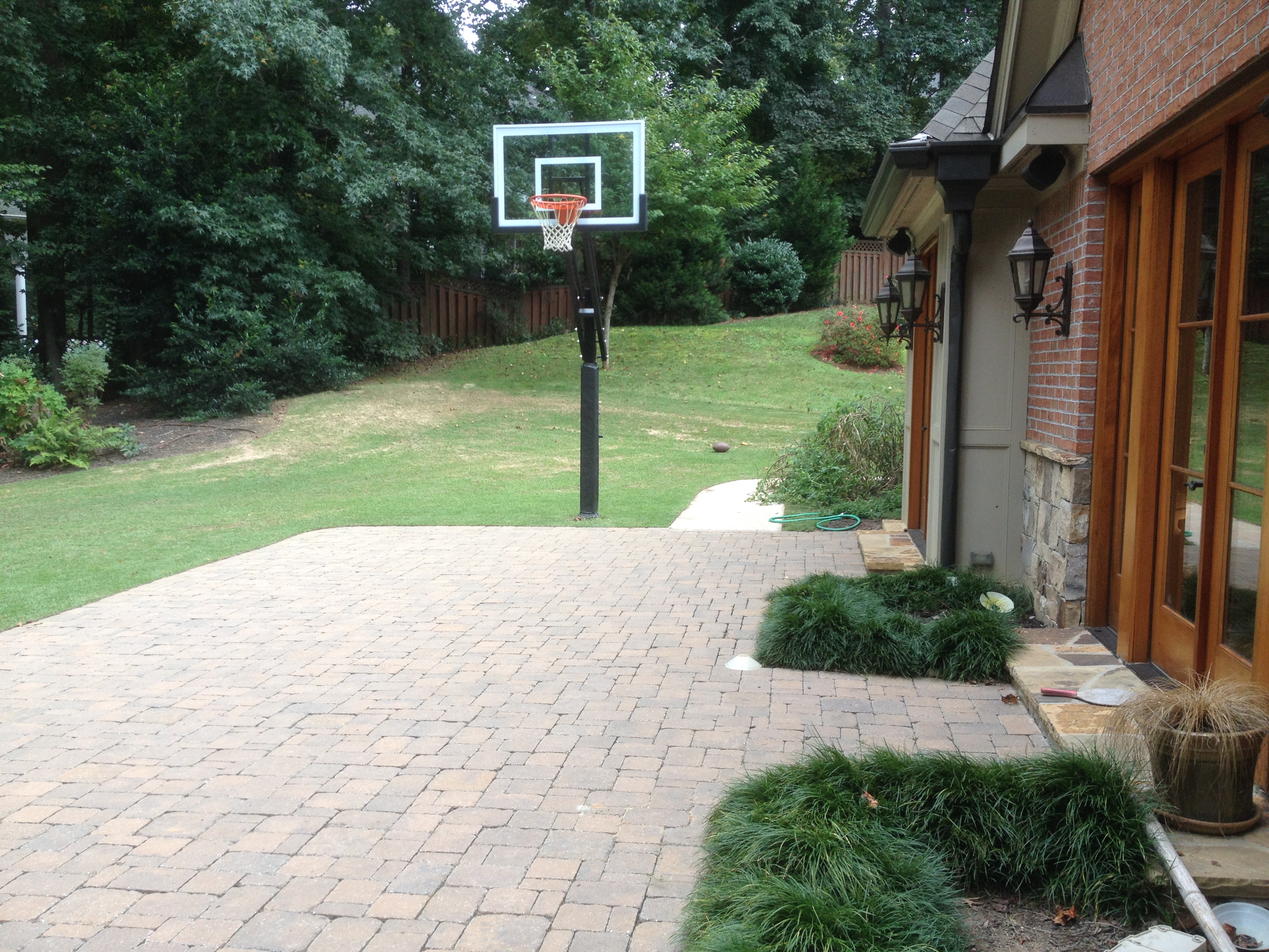 A pro dunk silver basketball system compliments the end of this cobbled brick backyard slab.
